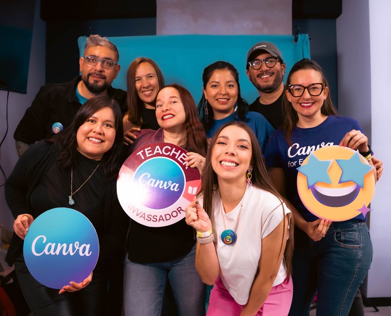 A diverse group of adults smiling and holding Canva branded signs, showcasing teamwork and creativity.