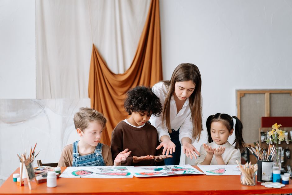A teacher guides children in a creative studio art class, focusing on hands-on painting.