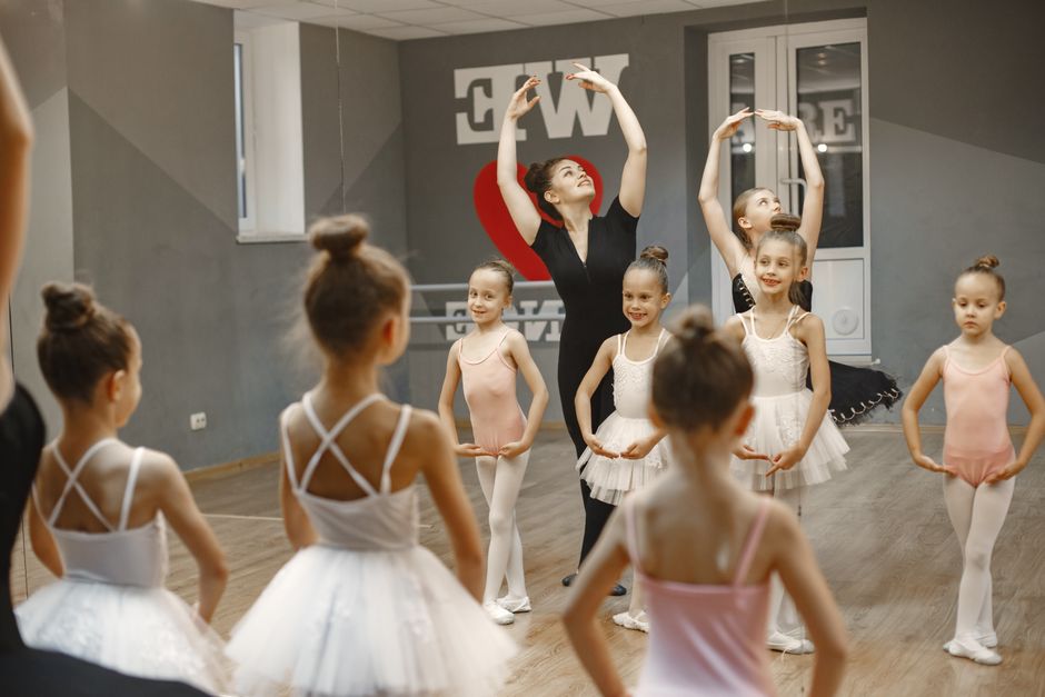 A group of young ballerinas practicing ballet poses under a teacher's guidance in a dance studio.
